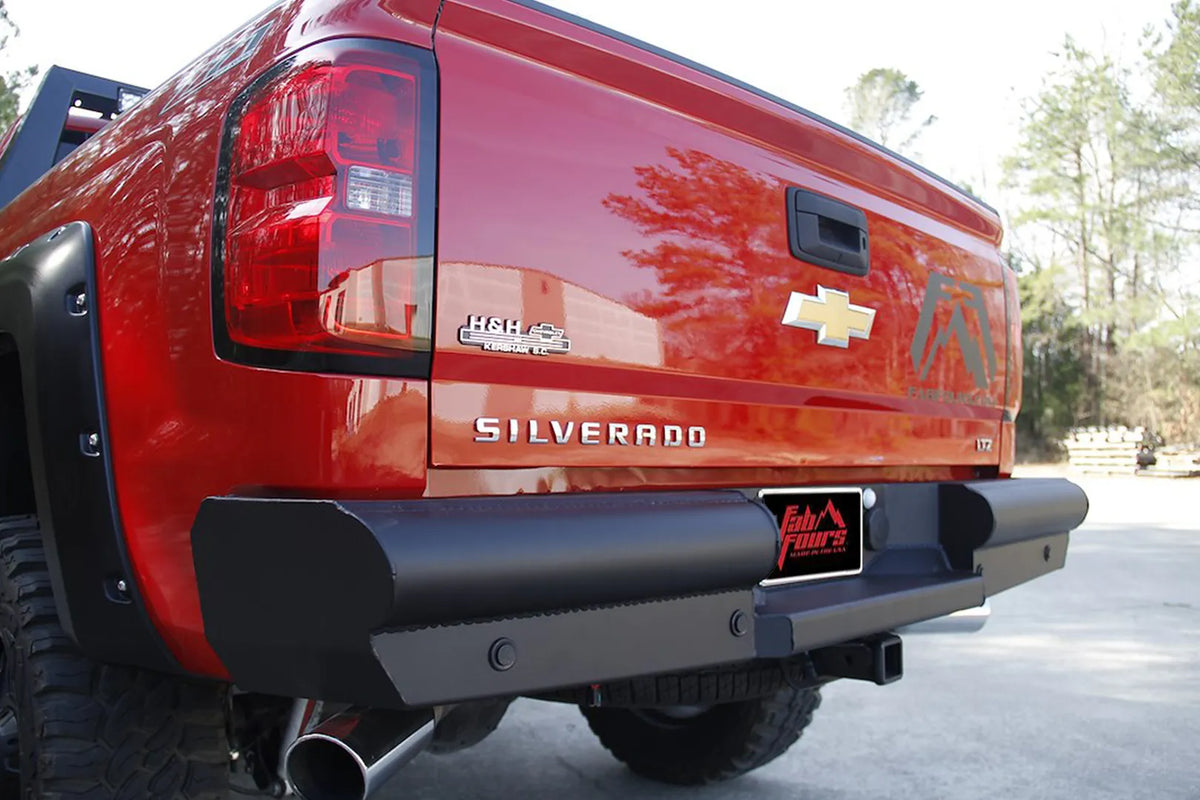 Fab Fours Black Steel Elite Rear Bumper on a red Chevrolet Silverado 1500 outdoors, close rear driver-side view of the flat black pipe bumper and plated end caps