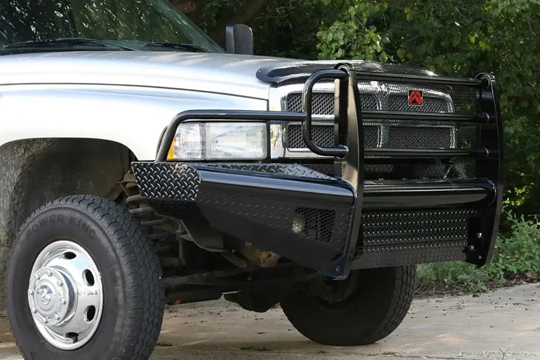 Fab Fours Black Steel front ranch bumper with full guard on a silver Ram 2500, front passenger-side three-quarter view outdoors, showing the full grille guard hoops, diamond-plate bumper face and integrated light openings