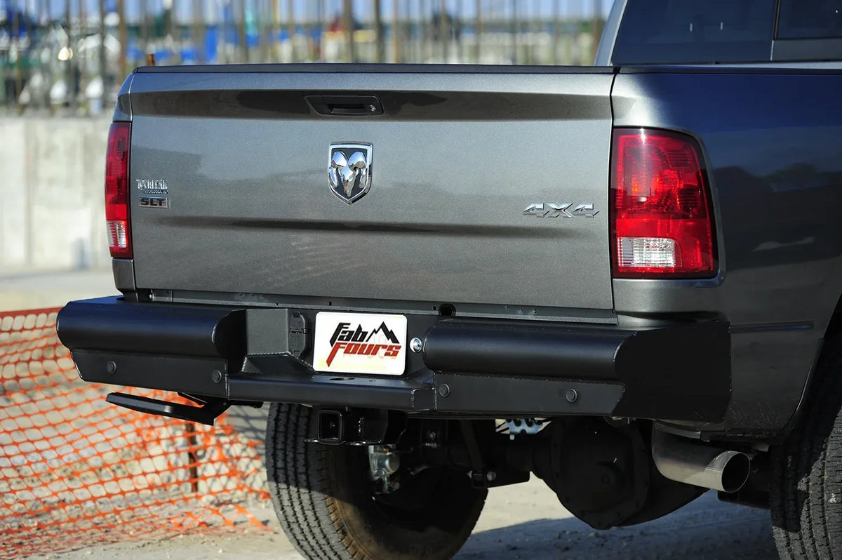 Fab Fours Black Steel Elite rear bumper on a gray Ram 2500, close-up rear view outdoors, showing the smooth bumper face, center plate pocket and hitch receiver