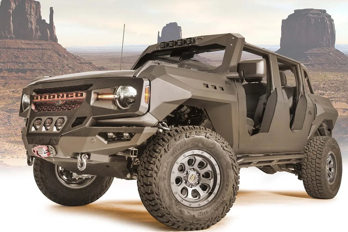 Fab Fours front steel fenders on a lifted gray Ford Bronco with doors removed, driver-side front three-quarter view with desert background, with Fab Fours winch bumper