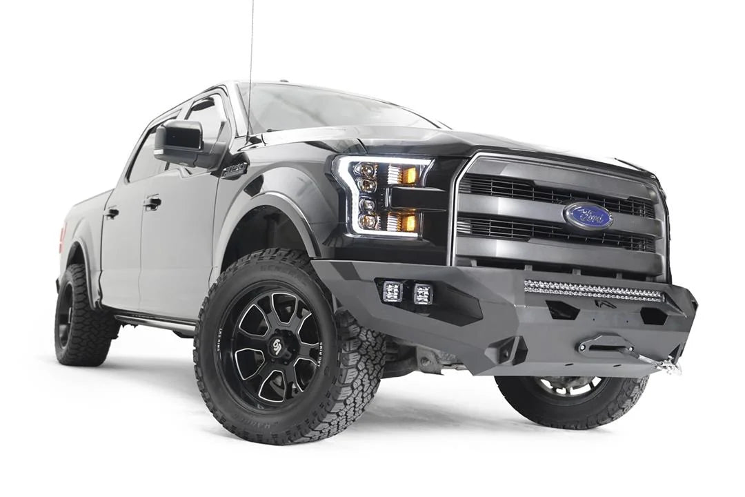 Fab Fours Matrix front bumper on a black Ford F-150, front passenger-side three-quarter view, showing the winch, light bar opening and cube light pods