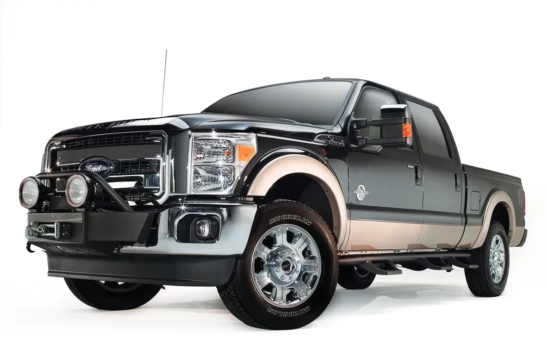 Fab Fours winch mount on a black and tan Ford Super Duty, front driver-side three-quarter view, showing the winch cradle behind the factory bumper and the light hoop with round lights