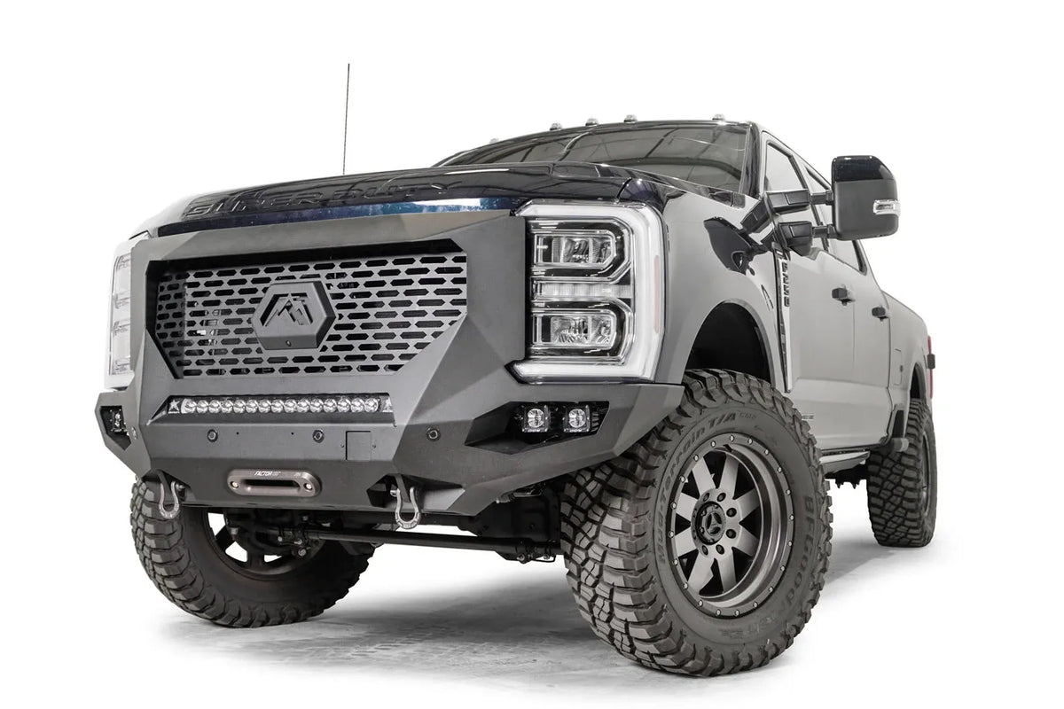 Fab Fours Grumper front winch bumper on a lifted dark blue 2023+ Ford Super Duty, front driver-side view, showing the full-height grille guard with the hex Fab Fours logo, the integrated LED light bar, pod lights and a centered winch fairlead with D-ring shackles