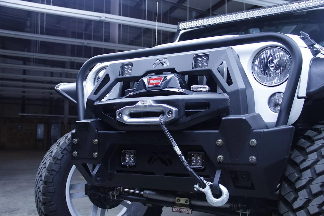 Fab Fours FMJ winch modifier installed on a white Jeep Wrangler JK with Warn winch, synthetic winch line, and cube lights, driver-side front angle