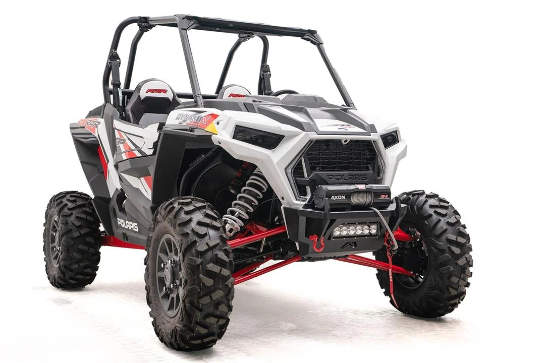 Fab Fours SxS winch bumper on a white Polaris RZR XP, passenger-side front three-quarter view, with Warn Axon winch, LED light bar, and red D-ring shackles