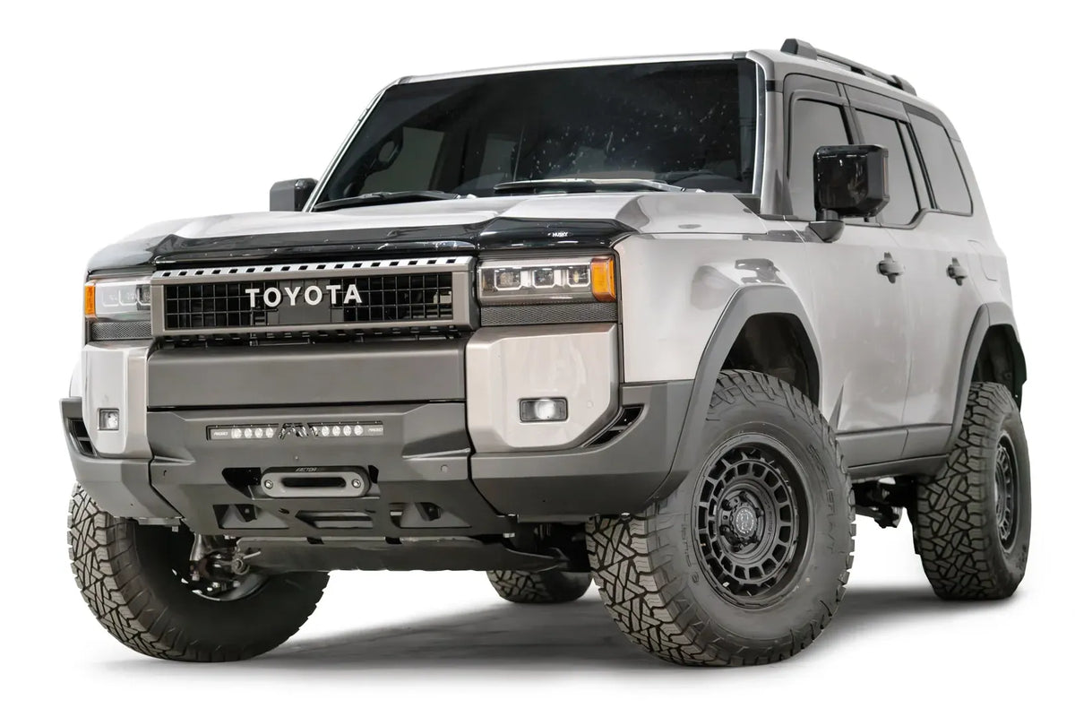 Fab Fours Hidden Winch Mount on a silver Toyota Land Cruiser, front three-quarter view from the driver side, showing the low-profile winch plate, LED light bar and fairlead