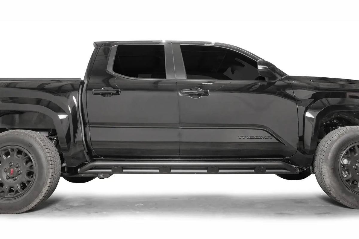 Fab Fours tube rock slider on a black Toyota Tacoma, passenger-side profile, showing the slider running