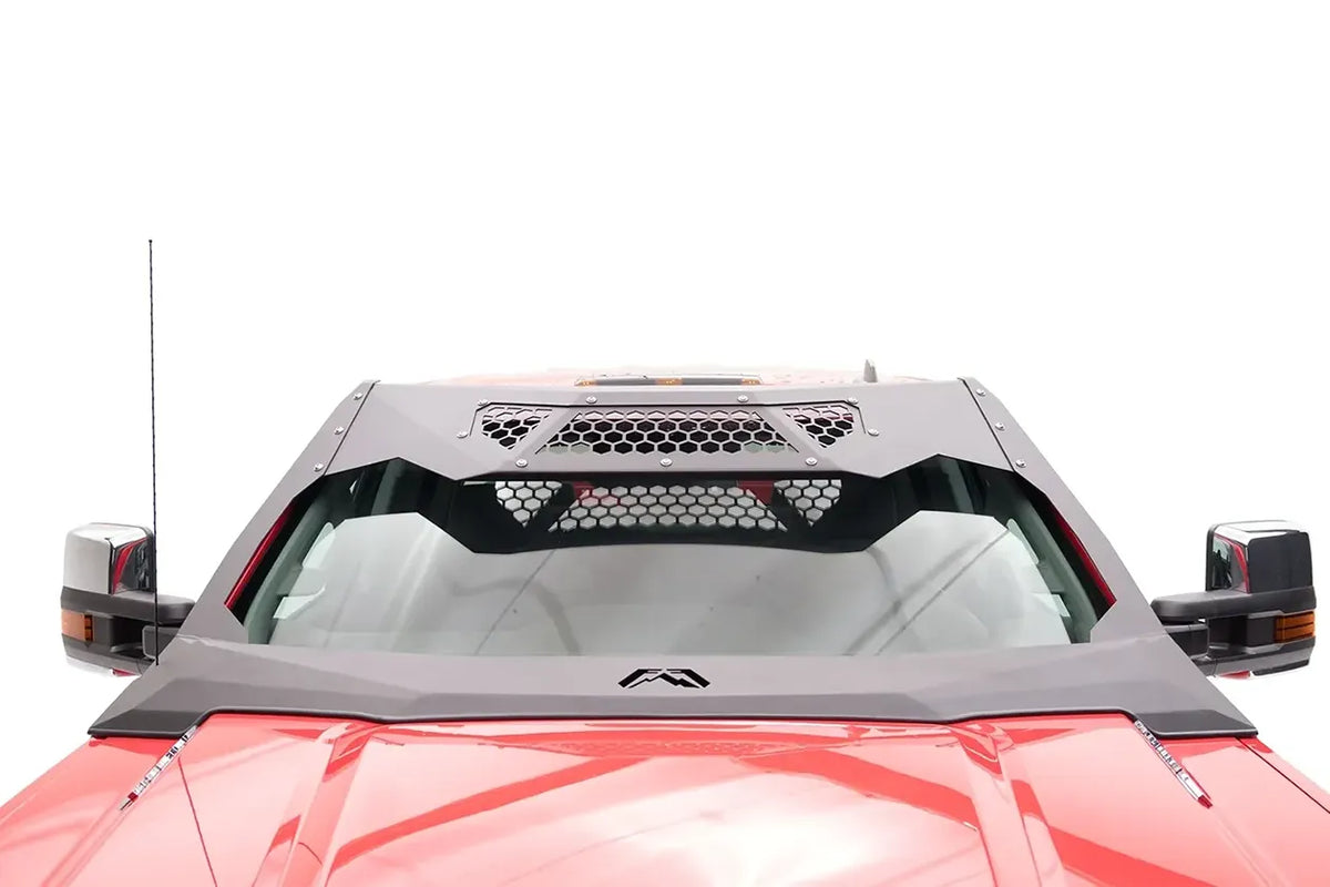 Fab Fours ViCowl on a red GMC Sierra HD, elevated front view over the hood, showing the angular steel cowl, honeycomb mesh roof visor and Fab Fours logo at the base of the windshield