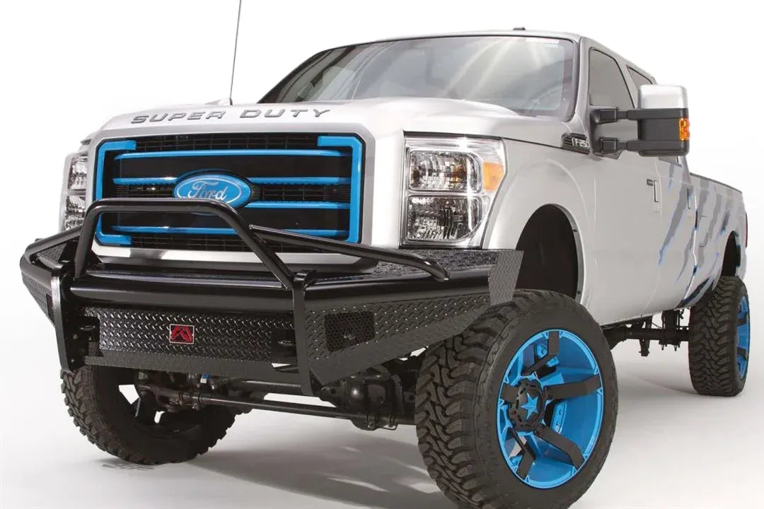 Fab Fours Black Steel front guard plate on a silver Ford Super Duty, front driver-side three-quarter view, showing the diamond-plate guard plate, pre-runner guard tubing and black steel front bumper