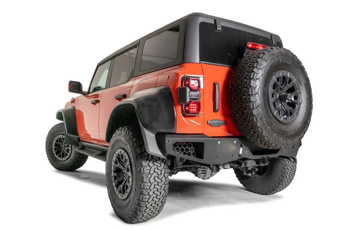 Fab Fours Vengeance rear bumper with honeycomb mesh corner openings on an orange Ford Bronco Raptor, driver-side rear three-quarter view