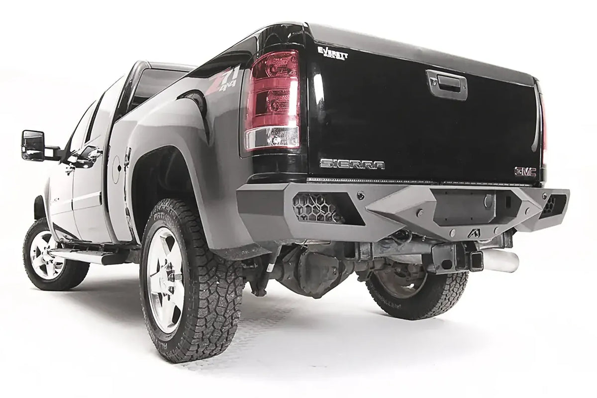 Fab Fours Vengeance rear bumper on a black GMC Sierra 2500HD, rear driver-side three-quarter view, showing the honeycomb light pods, angular end caps and Fab Fours logo