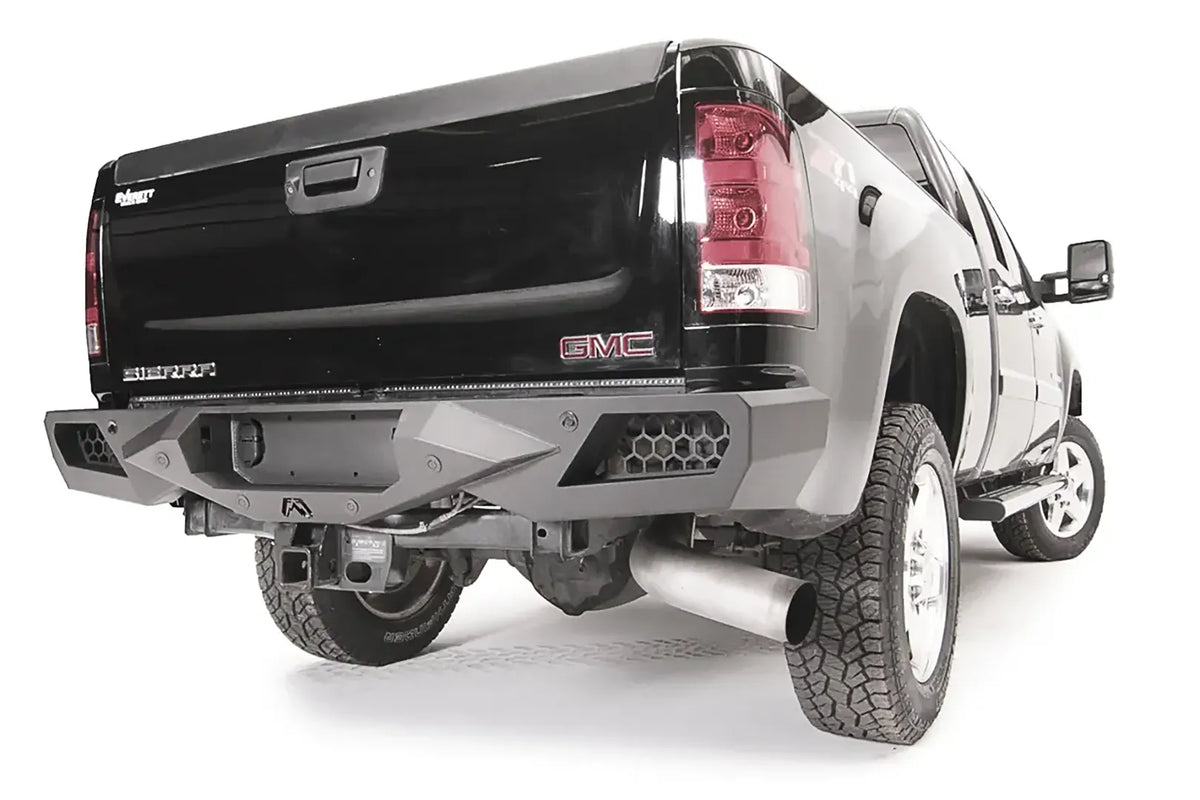 Fab Fours Vengeance rear bumper on a black GMC Sierra 2500HD, rear passenger-side three-quarter view, showing the honeycomb light pods, angular end caps and center hitch opening