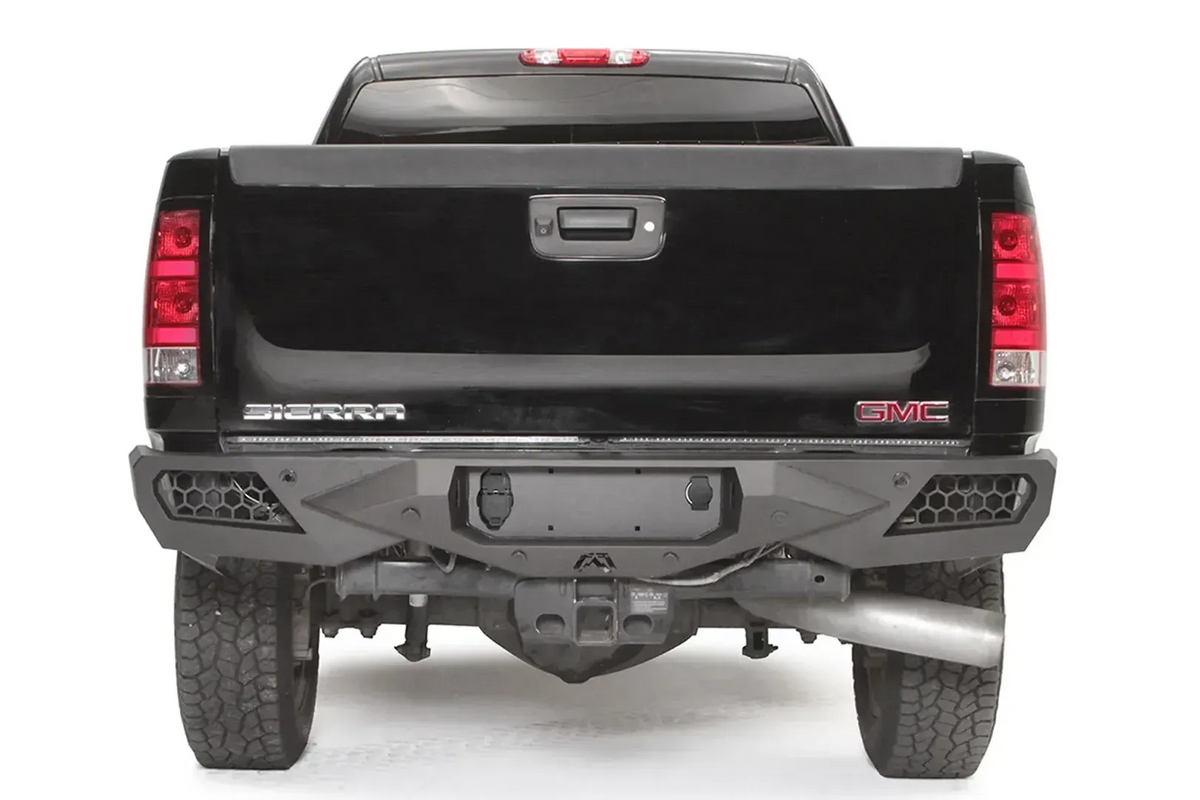 Fab Fours Vengeance rear bumper on a black GMC Sierra 2500HD, straight-on rear view, showing the honeycomb light pods, license plate recess and center hitch opening