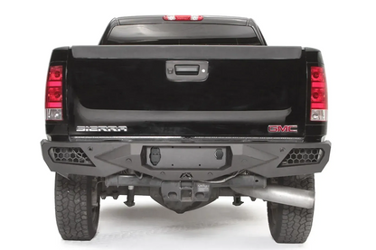 Fab Fours Vengeance rear bumper on a black GMC Sierra 2500HD, straight-on rear view, showing the honeycomb light pods, license plate recess and center hitch opening
