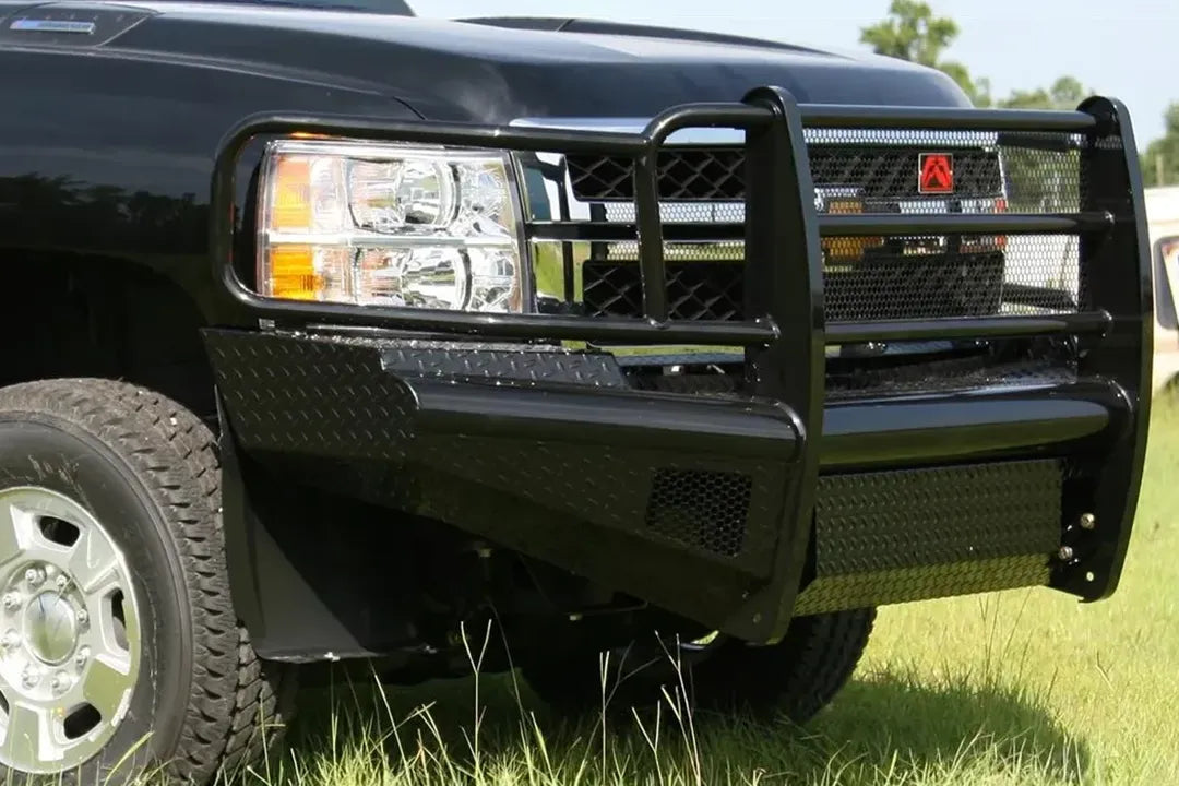 Fab Fours Black Steel front bumper with full guard on a black Chevrolet Silverado 2500HD, close-up front corner outdoor view, showing the full grille guard uprights, diamond-plate bumper top and mesh light opening