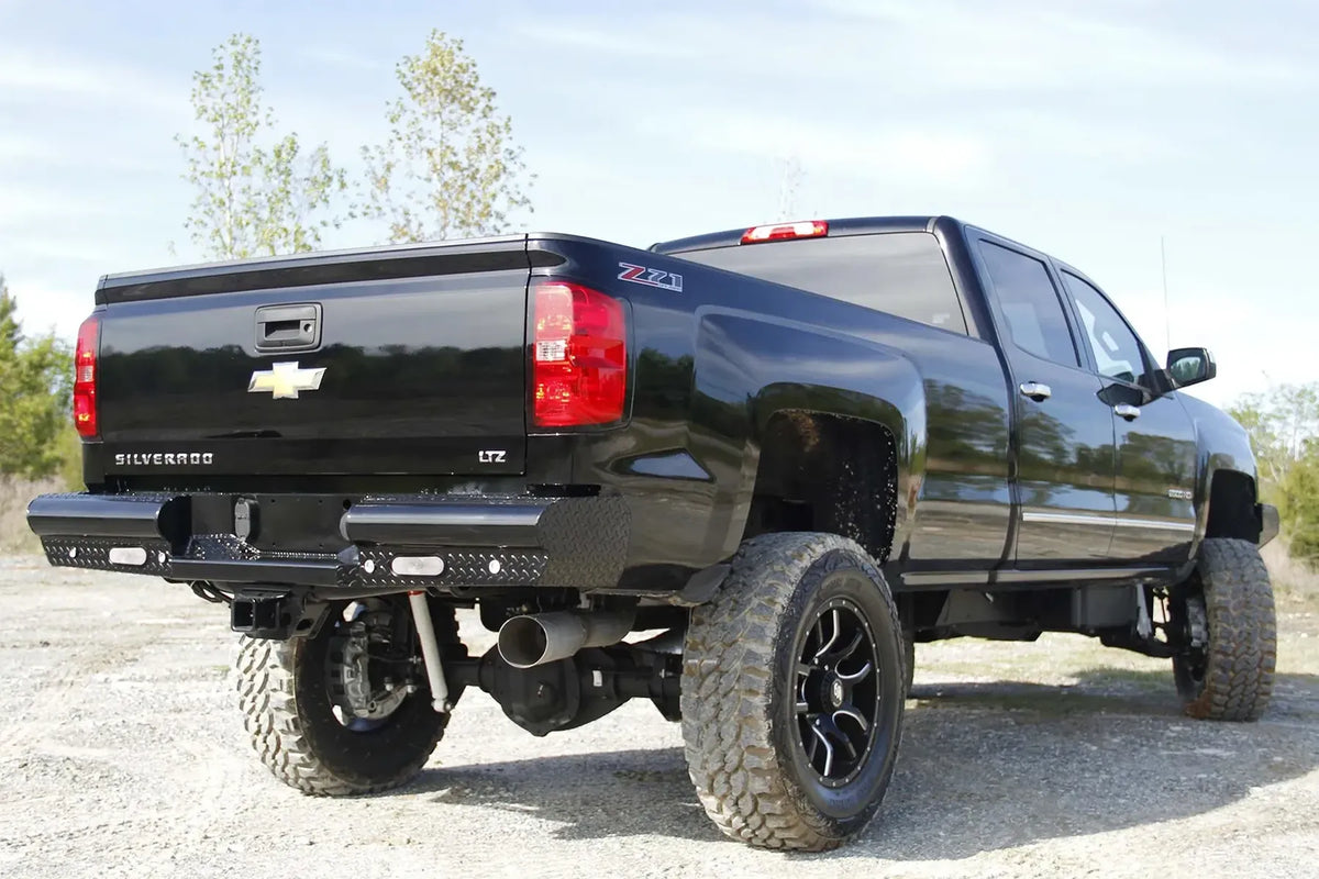 Fab Fours Black Steel rear bumper on a black Chevrolet Silverado 2500HD, rear passenger-side three-quarter outdoor view, showing the diamond-plate bumper face, integrated light cutouts and wrap-around end