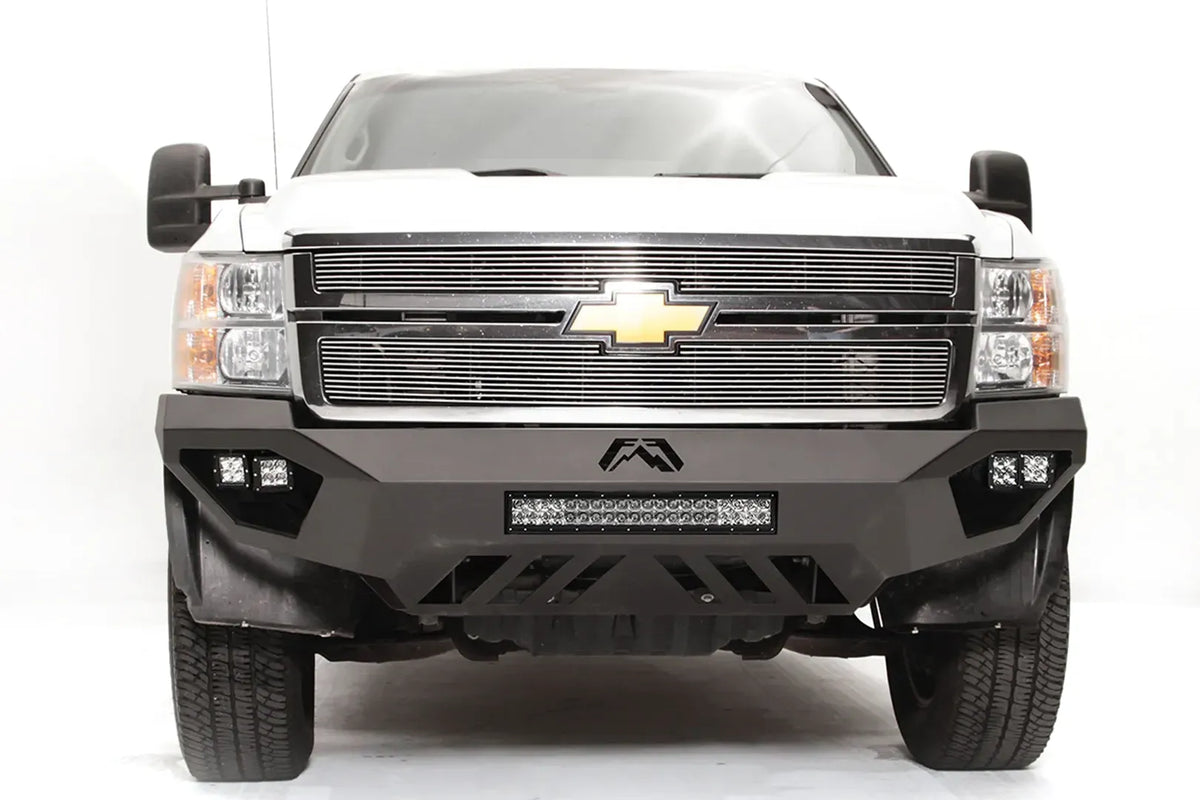 Fab Fours Vengeance front bumper on a white Chevrolet Silverado 2500HD, straight-on front view, showing the Fab Fours logo, cube light pods, center light bar and slotted skid plate