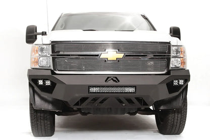 Fab Fours Vengeance front bumper on a white Chevrolet Silverado 2500HD, straight-on front view, showing the Fab Fours logo, cube light pods, center light bar and slotted skid plate
