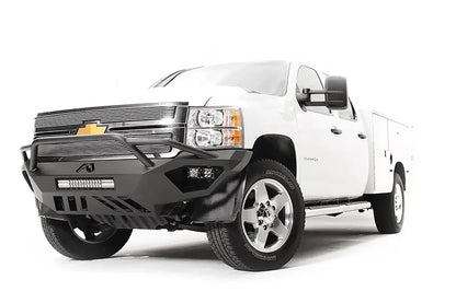 Fab Fours Vengeance front bumper with pre-runner guard on a white Chevrolet Silverado 2500HD, front driver-side three-quarter view, showing the pre-runner guard, cube light pods, center light bar opening and skid plate