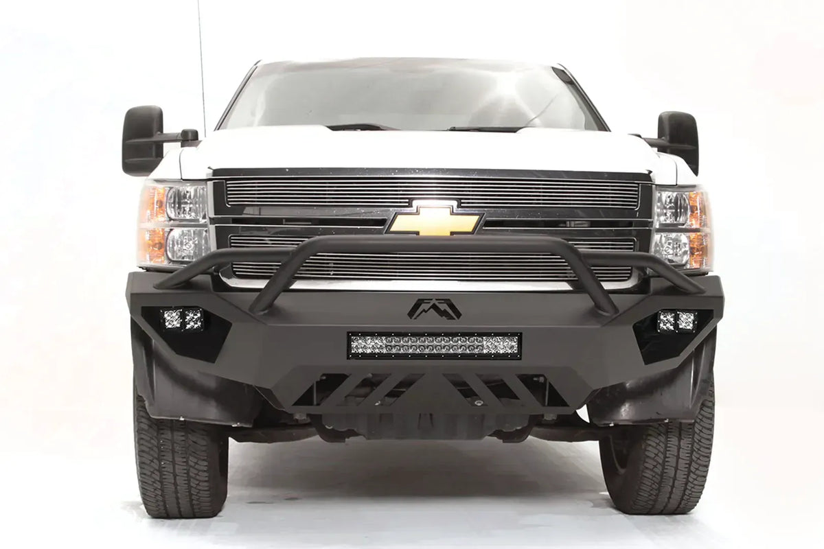 Fab Fours Vengeance front bumper with pre-runner guard on a white Chevrolet Silverado 2500HD, straight-on front view, showing the pre-runner guard tubing, Fab Fours logo, cube light pods and slotted skid plate