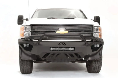 Fab Fours Vengeance front bumper with pre-runner guard on a white Chevrolet Silverado 2500HD, straight-on front view, showing the pre-runner guard tubing, Fab Fours logo, cube light pods and slotted skid plate