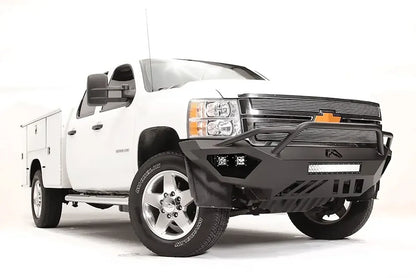 Fab Fours Vengeance front bumper with pre-runner guard on a white Chevrolet Silverado 2500HD, front passenger-side three-quarter view, showing the pre-runner guard, cube light pods, center light bar opening and skid plate
