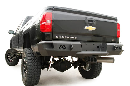 Fab Fours Premium rear bumper on a black Chevrolet Silverado 2500HD, rear driver-side three-quarter view, showing the Fab Fours logo cutouts, shackle mounts and angled bumper ends