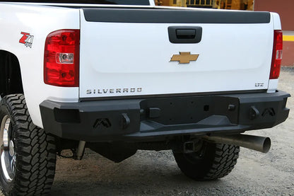 Fab Fours Premium rear bumper on a white Chevrolet Silverado 2500HD, close-up rear outdoor view, showing the Fab Fours logo cutouts, shackle mounts, recessed license plate area and hitch opening