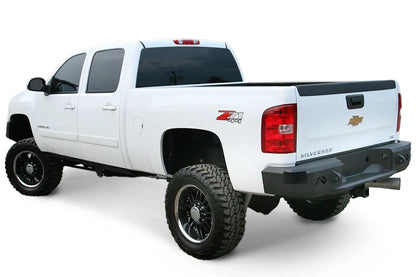 Fab Fours Premium rear bumper on a white Chevrolet Silverado 2500HD, rear driver-side three-quarter view, showing the angular bumper ends, Fab Fours logo cutouts and center step