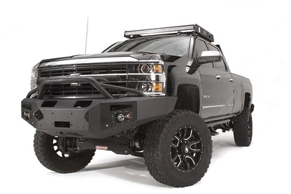 Fab Fours Premium Winch front bumper with pre-runner guard on a black Chevrolet Silverado 2500HD, front driver-side three-quarter view, showing the pre-runner guard, center winch plate, round lights and shackle mounts