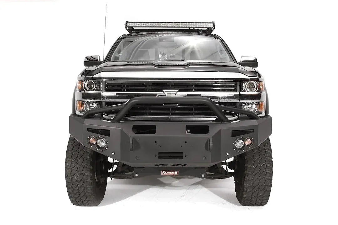Fab Fours Premium Winch front bumper with pre-runner guard on a black Chevrolet Silverado 2500HD, straight-on front view, showing the pre-runner guard tubing, center winch plate, round lights and shackle mounts
