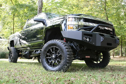 Fab Fours Premium Winch front bumper with pre-runner guard on a black Chevrolet Silverado 2500HD, front passenger-side three-quarter outdoor view, showing the pre-runner guard, center winch plate and round lights