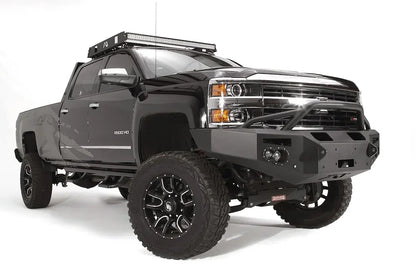 Fab Fours Premium Winch front bumper with pre-runner guard on a black Chevrolet Silverado 2500HD, front passenger-side three-quarter view, showing the pre-runner guard, center winch plate, round lights and shackle mounts