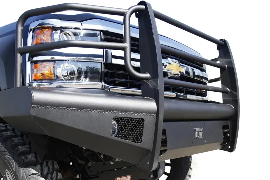 Fab Fours Black Steel Elite front bumper with full guard on a black Chevrolet Silverado 2500HD, close-up view on a white background, showing the full grille guard tubing, Elite badge and mesh light opening