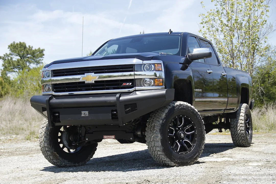 Fab Fours Black Steel Elite front bumper on a black Chevrolet Silverado 2500HD, front driver-side three-quarter outdoor view, showing the smooth-plate bumper face, Elite badge and wrap-around end caps