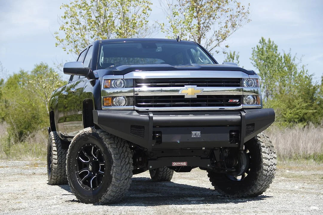Fab Fours Black Steel Elite front bumper on a black Chevrolet Silverado 2500HD, front outdoor view, showing the smooth-plate bumper face, Elite badge and mesh light openings