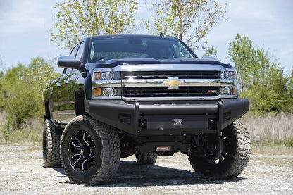 Fab Fours Black Steel Elite front bumper on a black Chevrolet Silverado 2500HD, front outdoor view, showing the smooth-plate bumper face, Elite badge and mesh light openings