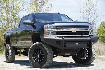 Fab Fours Black Steel Elite front bumper on a black Chevrolet Silverado 2500HD, front passenger-side three-quarter outdoor view, showing the smooth-plate bumper face, Elite badge and mesh light openings