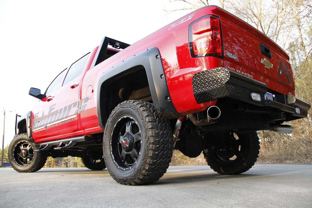 Fab Fours Black Steel rear bumper on a red Chevrolet Silverado, low rear driver-side three-quarter outdoor view, showing the diamond-plate end caps, integrated lights and center step