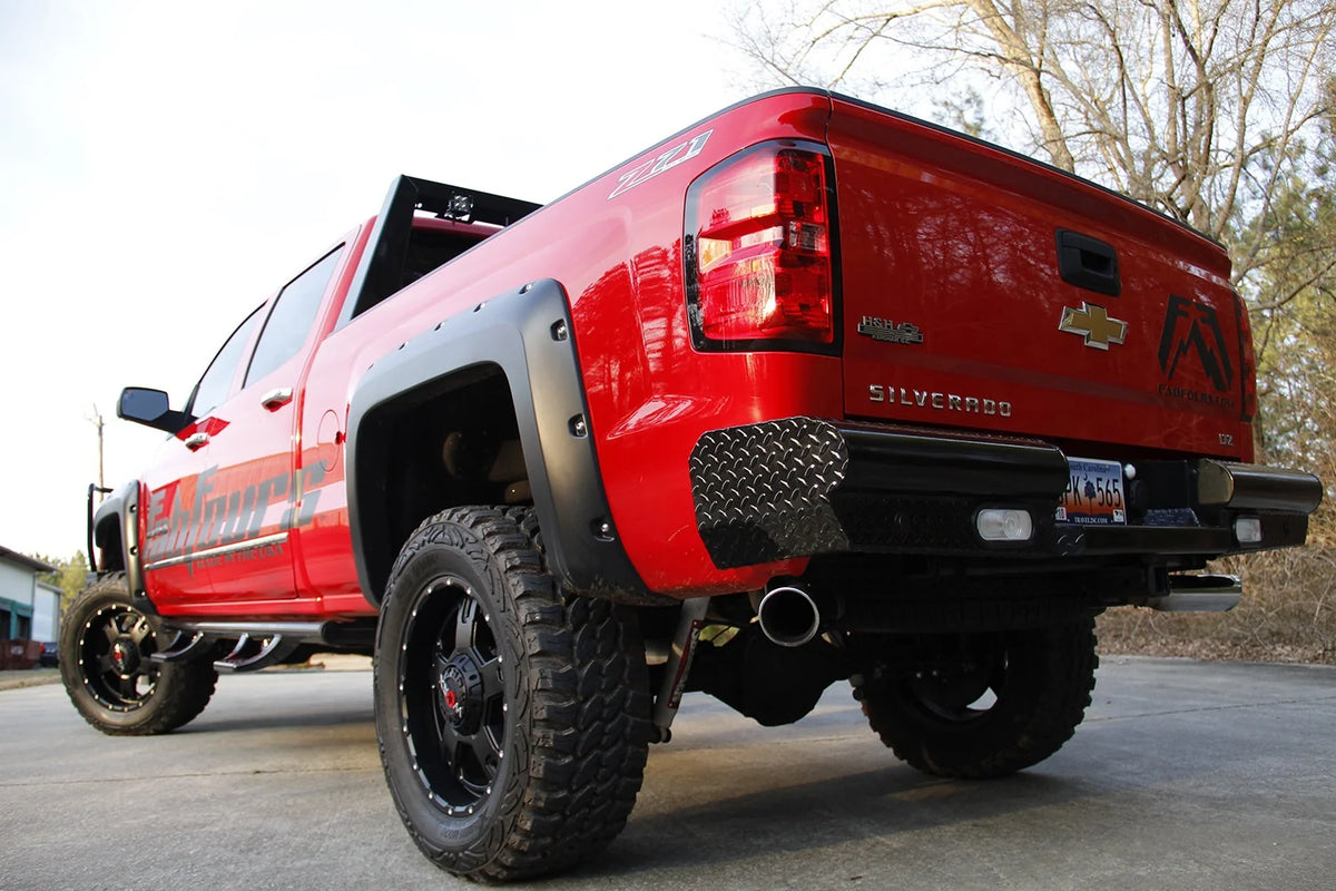 Fab Fours Black Steel rear bumper on a red Chevrolet Silverado, rear driver-side three-quarter outdoor view, showing the diamond-plate end caps, integrated lights and license plate recess