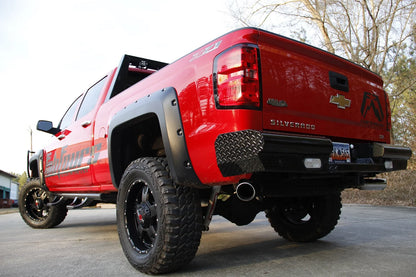 Fab Fours Black Steel rear bumper on a red Chevrolet Silverado, rear driver-side three-quarter outdoor view, showing the diamond-plate end caps, integrated lights and license plate recess