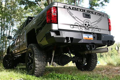 Fab Fours Premium rear bumper on a silver GMC Sierra 2500HD, rear driver-side three-quarter outdoor view, showing the square light cutouts, shackle mounts and angled bumper ends