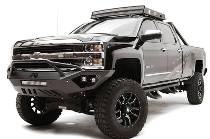Fab Fours Vengeance front bumper with pre-runner guard on a black Chevrolet Silverado 2500HD, front driver-side three-quarter view, showing the pre-runner guard, cube light pods, center light bar and skid plate