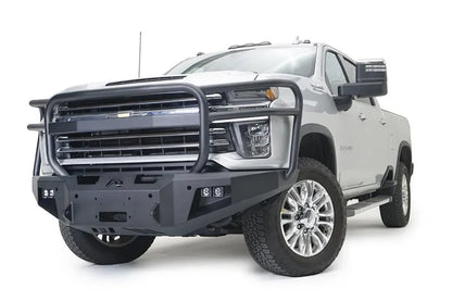 Fab Fours Premium Winch front bumper with full guard on a white Chevrolet Silverado 2500HD, front driver-side three-quarter view, showing the full grille guard, the center winch plate, cube light pods and Fab Fours logo