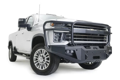 Fab Fours Premium Winch front bumper with full guard on a white Chevrolet Silverado 2500HD, front passenger-side three-quarter view, showing the full grille guard, the center winch plate, cube light pods and angular bumper ends