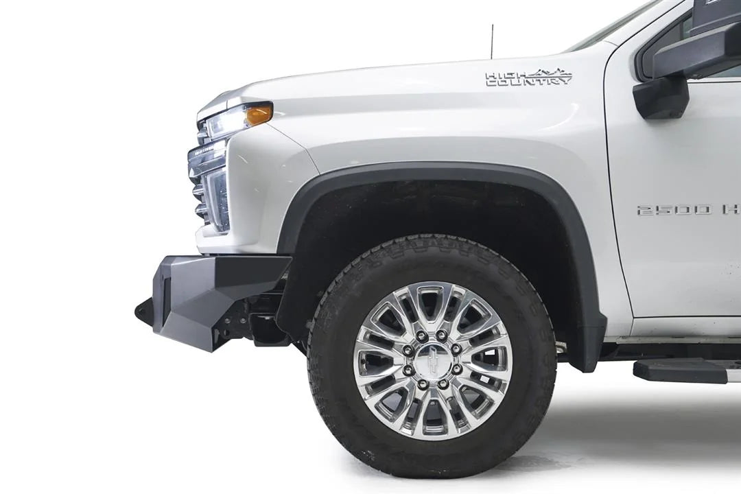 Fab Fours Premium Winch front bumper on a white Chevrolet Silverado 2500HD, close-up front corner view from the driver side, showing the angular bumper end and wheel clearance