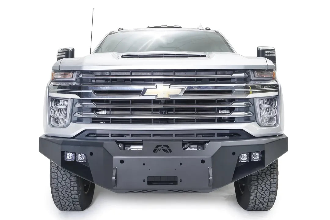 Fab Fours Premium Winch front bumper on a white Chevrolet Silverado 2500HD, straight-on front view, showing the center winch plate, Fab Fours logo and cube light pods