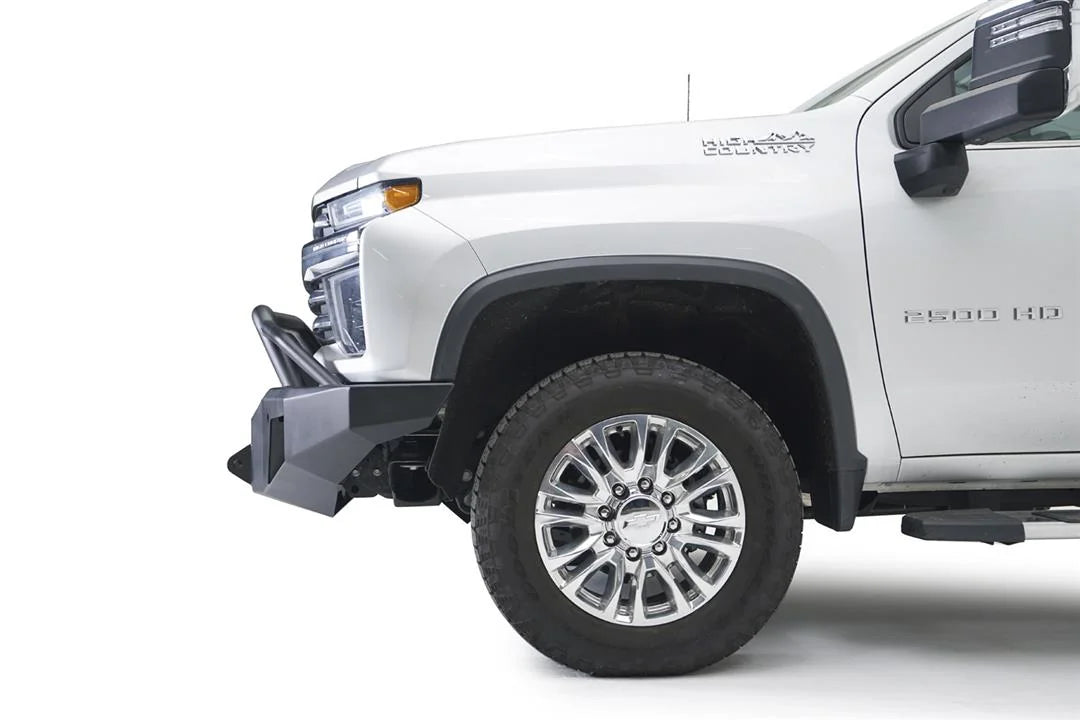 Fab Fours Premium Winch front bumper with pre-runner guard on a white Chevrolet Silverado 2500HD, close-up front corner view from the driver side, showing the pre-runner guard, the angular bumper end and wheel clearance