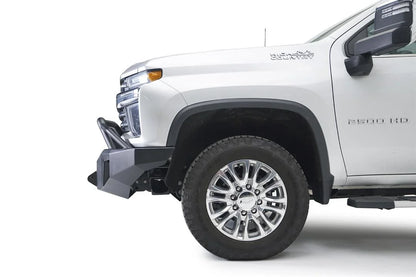 Fab Fours Premium Winch front bumper with pre-runner guard on a white Chevrolet Silverado 2500HD, close-up front corner view from the driver side, showing the pre-runner guard, the angular bumper end and wheel clearance