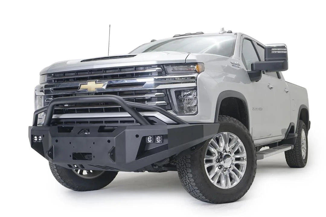 Fab Fours Premium Winch front bumper with pre-runner guard on a white Chevrolet Silverado 2500HD, front driver-side three-quarter view, showing the pre-runner guard, the center winch plate, cube light pods and Fab Fours logo